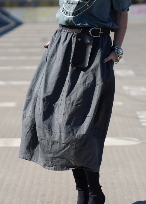 Grafitowa spódnica damska o kroju bombki z kieszeniami i dekoracyjnymi przeszyciami, pokazana w stylizacji z zielonym swetrem i czarnymi botkami na obcasie.