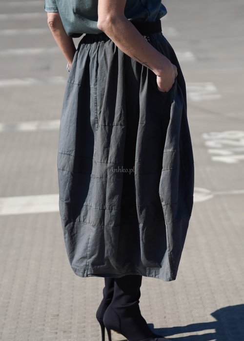 Grafitowa spódnica damska o kroju bombki z kieszeniami i dekoracyjnymi przeszyciami, pokazana w stylizacji z zielonym swetrem i czarnymi botkami na obcasie.