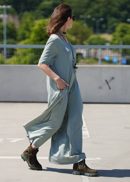 Kombinezon damski oversize w kolorze khaki z szerokimi nogawkami i wycięciem na plecach, stylizacja miejska z paskiem i biżuterią.