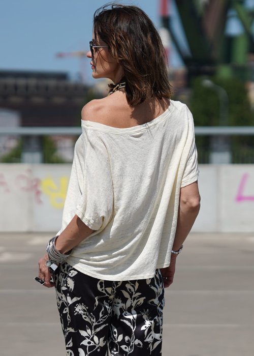 Lniana bluzka damska Alga w kolorze cream z szerokim dekoltem i luźnym fasonem oversize, zestawiona ze wzorzystymi spodniami.