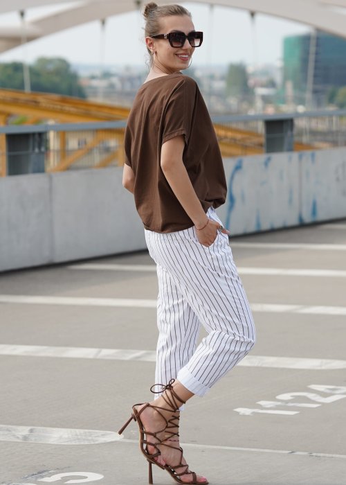 Brązowa bluzka damska oversize z krótkim rękawem i szerokim dekoltem w codziennej stylizacji z jasnymi spodniami w paski.