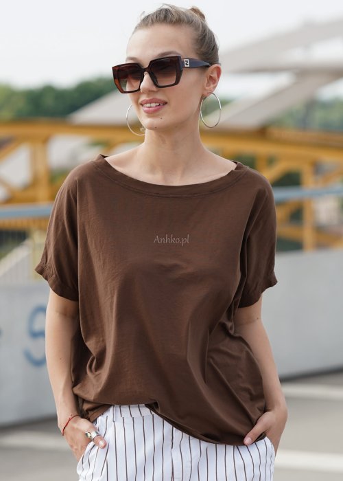 Brązowa bluzka damska oversize z krótkim rękawem i szerokim dekoltem w codziennej stylizacji z jasnymi spodniami w paski.