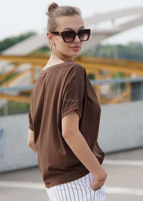 Brązowa bluzka damska oversize z krótkim rękawem i szerokim dekoltem w codziennej stylizacji z jasnymi spodniami w paski.