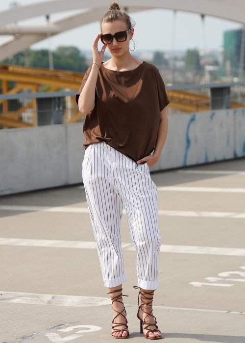 Brązowa bluzka damska oversize z krótkim rękawem i szerokim dekoltem w codziennej stylizacji z jasnymi spodniami w paski.