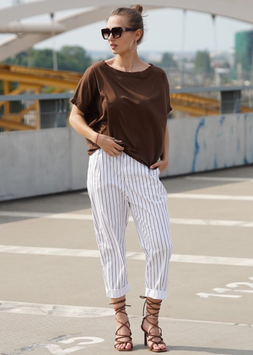 Brązowa bluzka damska oversize z krótkim rękawem i szerokim dekoltem w codziennej stylizacji z jasnymi spodniami w paski.