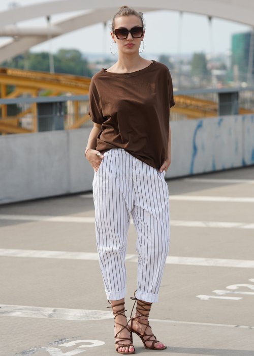 Brązowa bluzka damska oversize z krótkim rękawem i szerokim dekoltem w codziennej stylizacji z jasnymi spodniami w paski.