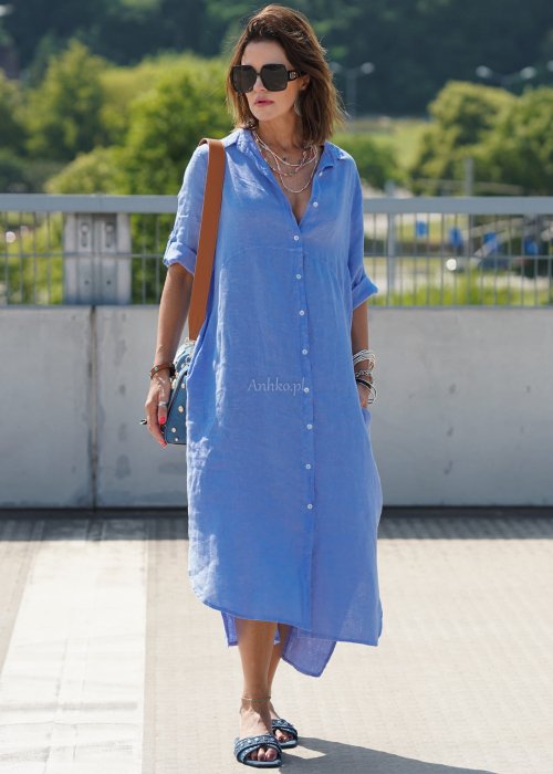 Niebieska lniana sukienka maxi w stylu szmizjerki, zapinana na guziki, o luźnym fasonie oversize, stylizowana z sandałami i torebką na ramię.