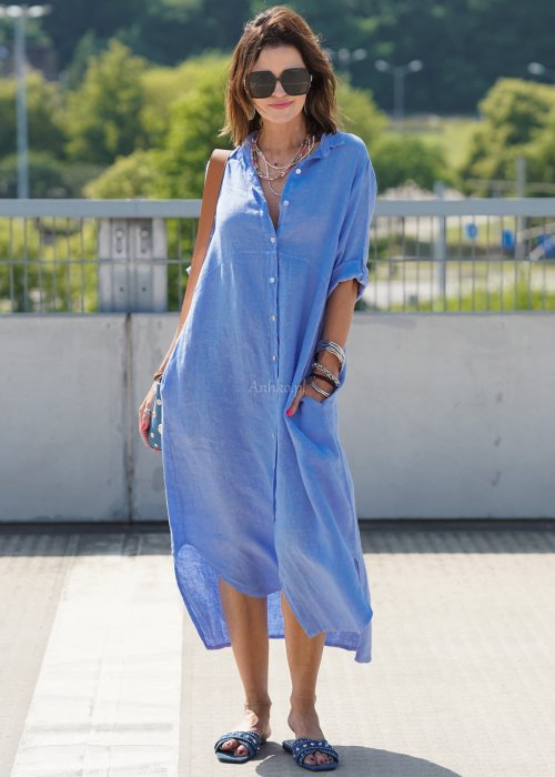 Niebieska lniana sukienka maxi w stylu szmizjerki, zapinana na guziki, o luźnym fasonie oversize, stylizowana z sandałami i torebką na ramię.