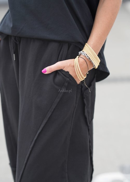 Czarne spodnie dresowe damskie o luźnym kroju baggy z ozdobnymi przeszyciami i gumką w pasie, stylizowane ze sneakersami w miejskim looku.