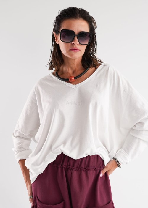 Biała bluzka damska oversize z długim rękawem i dekoltem V w stylizacji z jeansami i różowym naszyjnikiem.