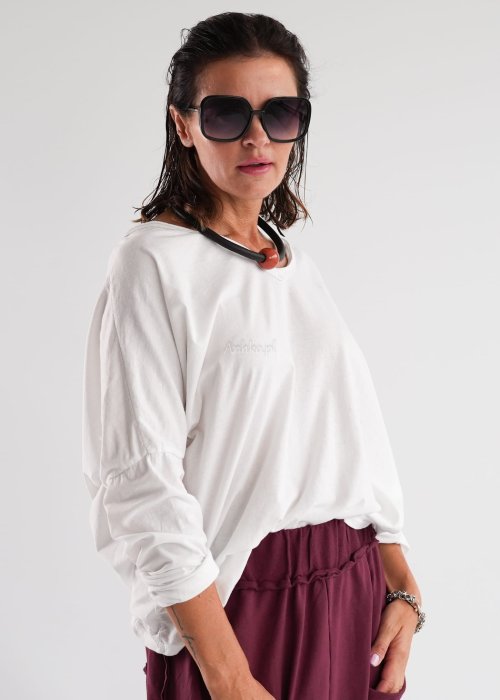 Biała bluzka damska oversize z długim rękawem i dekoltem V w stylizacji z jeansami i różowym naszyjnikiem.