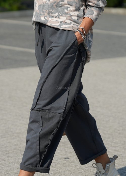 Szare spodnie damskie oversize z ozdobnymi przeszyciami i elastycznym pasem. Stylizacja z bluzką w print i jasnymi botkami w miejskim stylu.