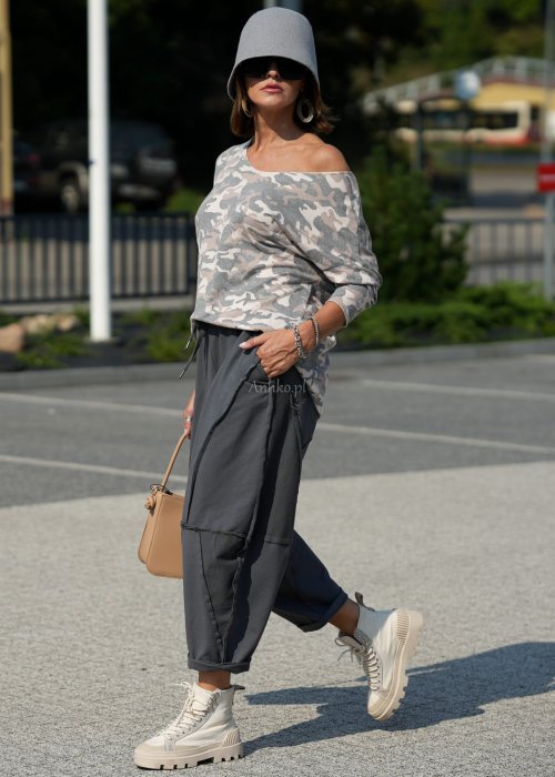 Szare spodnie damskie oversize z ozdobnymi przeszyciami i elastycznym pasem. Stylizacja z bluzką w print i jasnymi botkami w miejskim stylu.