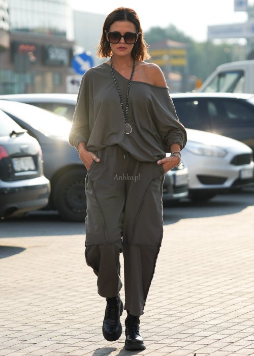 Bluzka damska oversize w kolorze taupe z szerokim dekoltem odsłaniającym ramię, wykonana z bawełny. Stylizacja casual z dodatkami i spodniami.