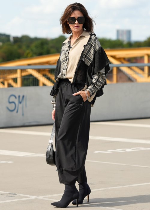 Czarne spodnie damskie z szeroką nogawką i efektem bombki, z elastycznym pasem. Stylizacja z botkami na obcasie w nowoczesnym, miejskim stylu.