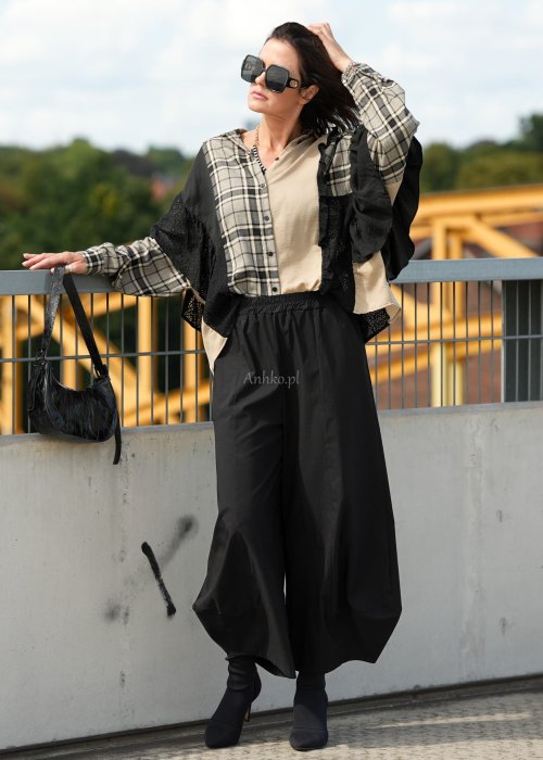 Czarne spodnie damskie z szeroką nogawką i efektem bombki, z elastycznym pasem. Stylizacja z botkami na obcasie w nowoczesnym, miejskim stylu.