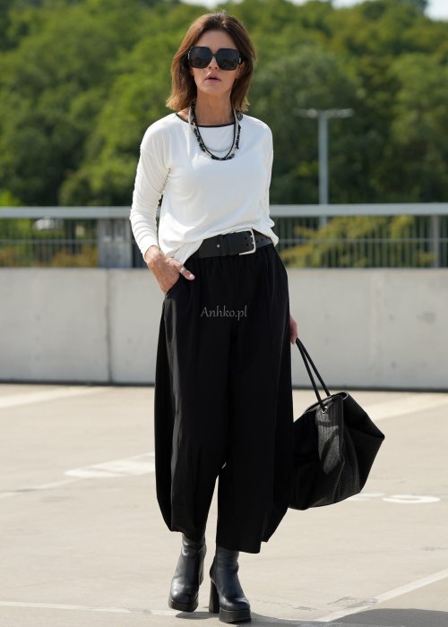 Czarne spodnie damskie z szeroką nogawką i efektem bombki, z elastycznym pasem. Stylizacja z botkami na obcasie w nowoczesnym, miejskim stylu.