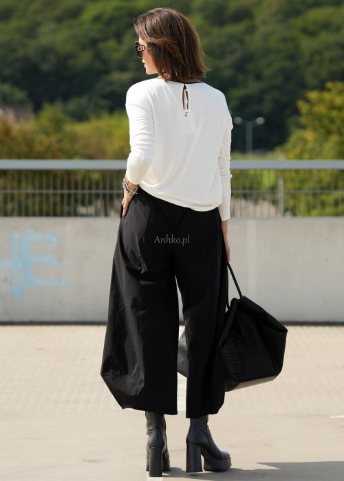 Czarne spodnie damskie z szeroką nogawką i efektem bombki, z elastycznym pasem. Stylizacja z botkami na obcasie w nowoczesnym, miejskim stylu.