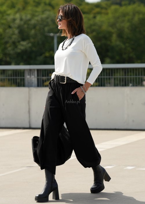 Czarne spodnie damskie z szeroką nogawką i efektem bombki, z elastycznym pasem. Stylizacja z botkami na obcasie w nowoczesnym, miejskim stylu.