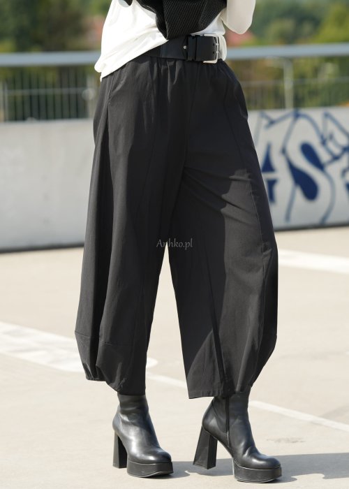 Czarne spodnie damskie z szeroką nogawką i efektem bombki, z elastycznym pasem. Stylizacja z botkami na obcasie w nowoczesnym, miejskim stylu.