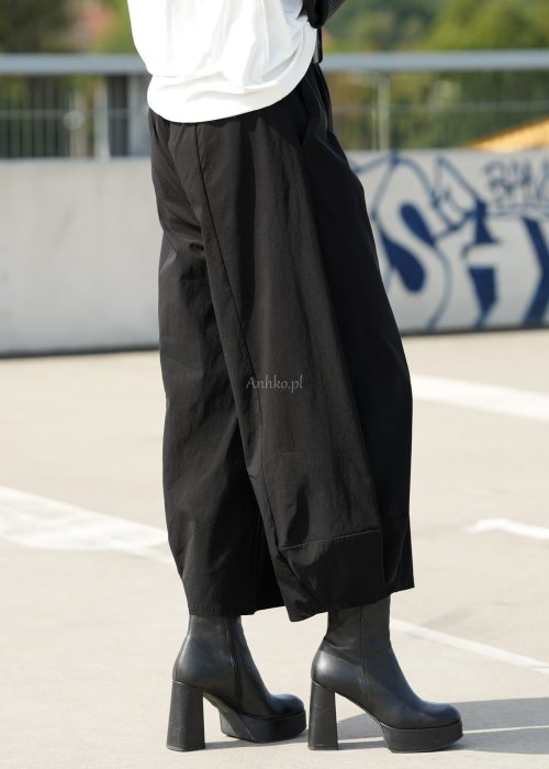 Czarne spodnie damskie z szeroką nogawką i efektem bombki, z elastycznym pasem. Stylizacja z botkami na obcasie w nowoczesnym, miejskim stylu.