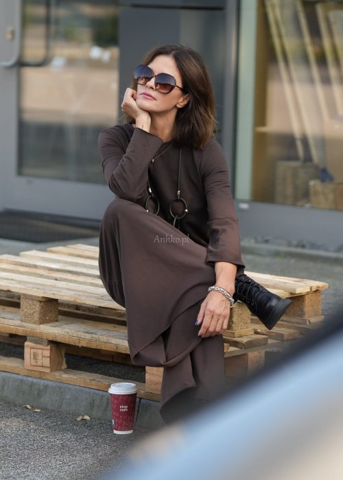 Brązowy kombinezon damski z długim rękawem i bardzo szeroką nogawką, luźny fason z półokrągłym dekoltem w miejskiej stylizacji z botkami.