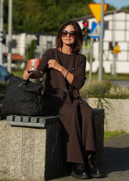 Brązowy kombinezon damski z długim rękawem i bardzo szeroką nogawką, luźny fason z półokrągłym dekoltem w miejskiej stylizacji z botkami.