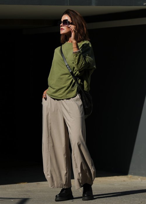 Zielona bluza oversize Nora z obniżoną linią ramion, długimi rękawami i dekoracyjną naszywką przy dole, zestawiona ze spodniami w podobnej tonacji.