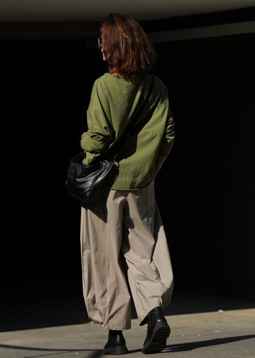 Zielona bluza oversize Nora z obniżoną linią ramion, długimi rękawami i dekoracyjną naszywką przy dole, zestawiona ze spodniami w podobnej tonacji.
