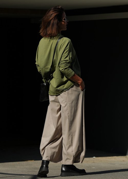 Zielona bluza oversize Nora z obniżoną linią ramion, długimi rękawami i dekoracyjną naszywką przy dole, zestawiona ze spodniami w podobnej tonacji.