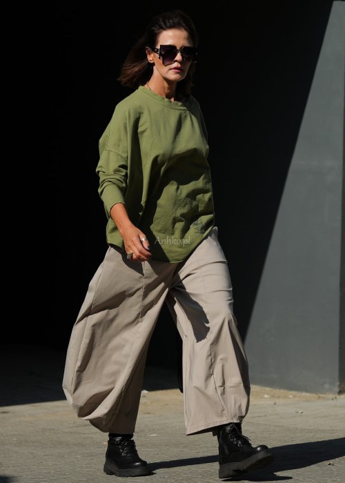 Zielona bluza oversize Nora z obniżoną linią ramion, długimi rękawami i dekoracyjną naszywką przy dole, zestawiona ze spodniami w podobnej tonacji.