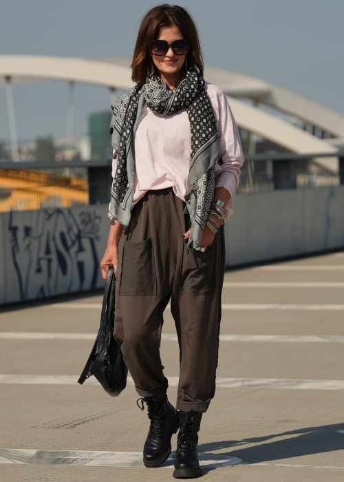 Pudroworóżowa bluzka damska oversize z długim rękawem i dekoltem V. Model pokazany w stylizacji z ciemną spódnicą i biżuterią, w miejskim otoczeniu.