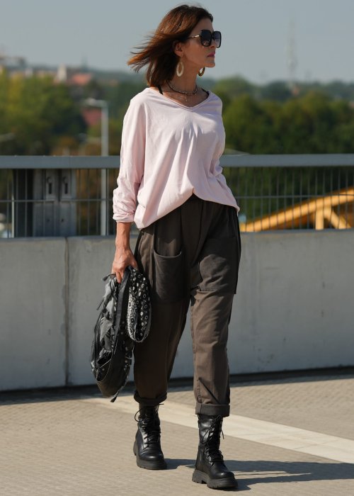 Pudroworóżowa bluzka damska oversize z długim rękawem i dekoltem V. Model pokazany w stylizacji z ciemną spódnicą i biżuterią, w miejskim otoczeniu.
