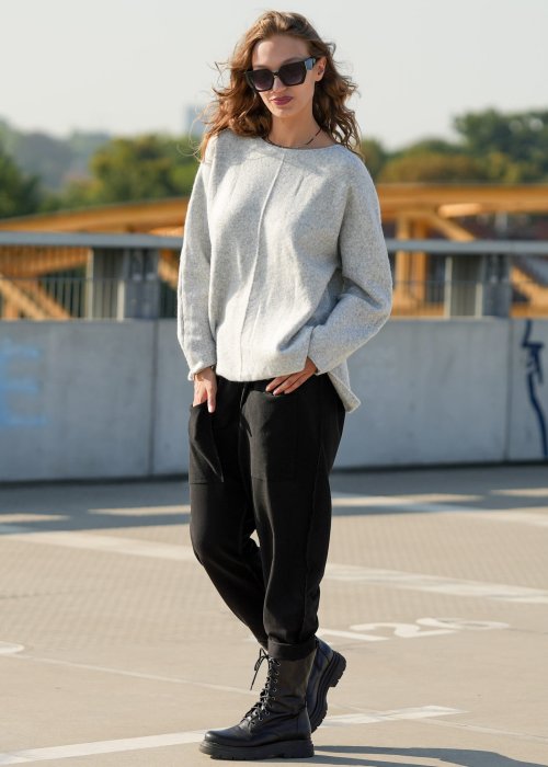 Czarne spodnie damskie o luźnym kroju z dużymi naszywanymi kieszeniami, zestawione z szarym swetrem i czarnymi botkami w miejskiej stylizacji.
