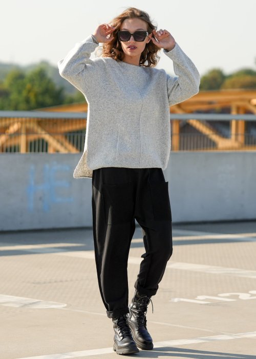 Czarne spodnie damskie o luźnym kroju z dużymi naszywanymi kieszeniami, zestawione z szarym swetrem i czarnymi botkami w miejskiej stylizacji.