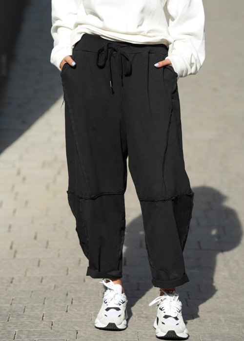 Czarne spodnie dresowe damskie o luźnym kroju baggy z ozdobnymi przeszyciami i gumką w pasie, stylizowane ze sneakersami w miejskim looku.