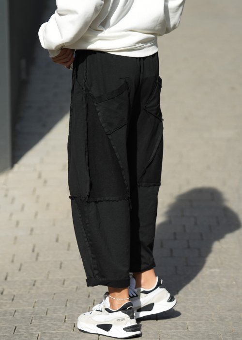 Czarne spodnie dresowe damskie o luźnym kroju baggy z ozdobnymi przeszyciami i gumką w pasie, stylizowane ze sneakersami w miejskim looku.