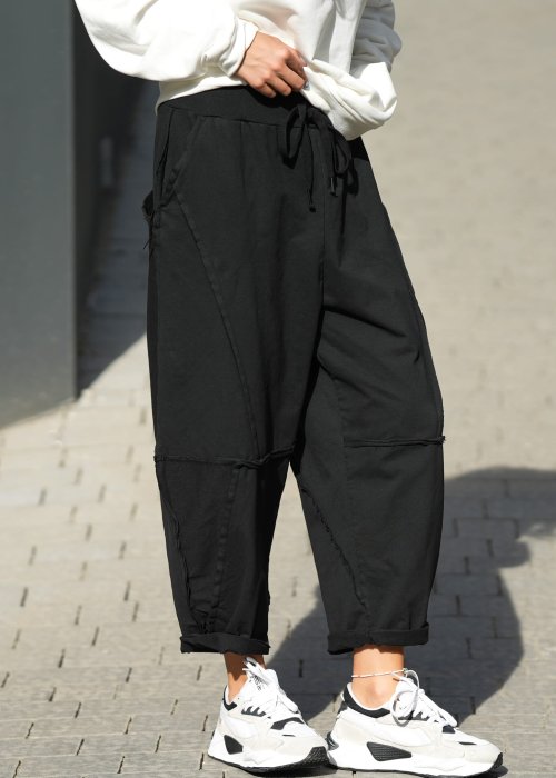 Czarne spodnie dresowe damskie o luźnym kroju baggy z ozdobnymi przeszyciami i gumką w pasie, stylizowane ze sneakersami w miejskim looku.