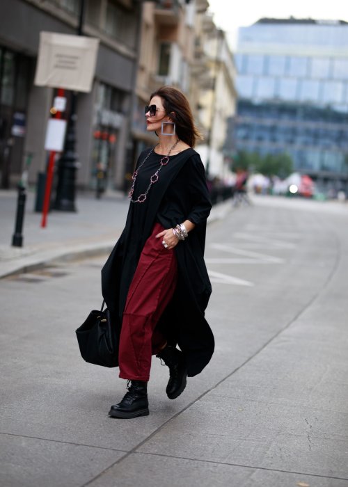 Bordowe spodnie dresowe damskie z obniżonym krokiem i ozdobnymi przeszyciami, luźny fason z gumką w pasie i sznurkiem, stylizacja miejska z czarnymi botkami.