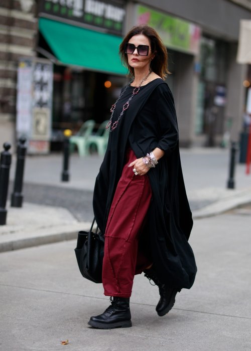 Bordowe spodnie dresowe damskie z obniżonym krokiem i ozdobnymi przeszyciami, luźny fason z gumką w pasie i sznurkiem, stylizacja miejska z czarnymi botkami.