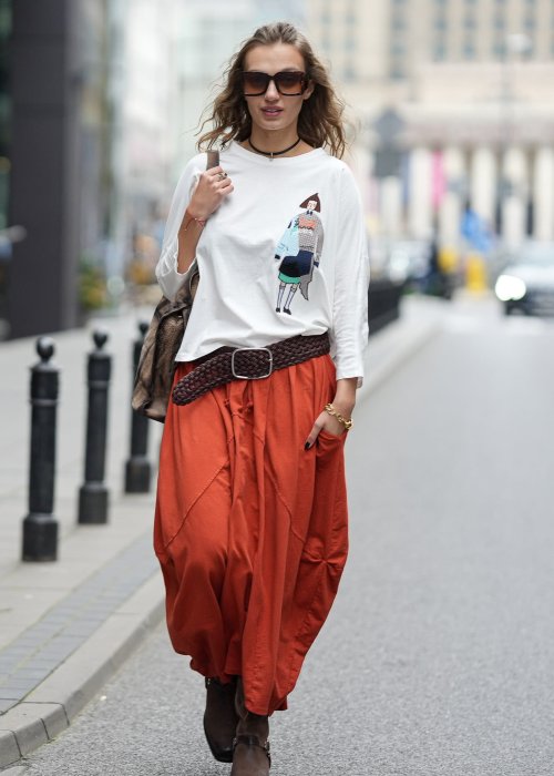 Ceglana spódnica maxi typu bombka z elastycznym pasem i przeszyciami, zestawiona z jasną bluzką i botkami w miejskiej stylizacji.