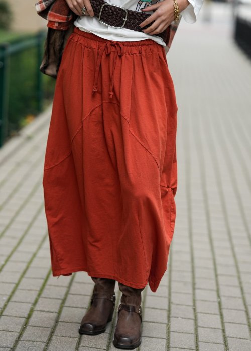 Ceglana spódnica maxi typu bombka z elastycznym pasem i przeszyciami, zestawiona z jasną bluzką i botkami w miejskiej stylizacji.