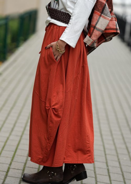 Ceglana spódnica maxi typu bombka z elastycznym pasem i przeszyciami, zestawiona z jasną bluzką i botkami w miejskiej stylizacji.