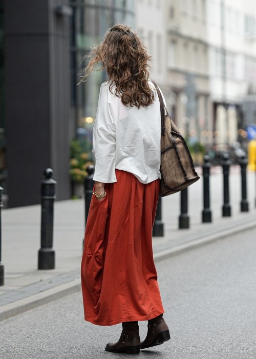 Ceglana spódnica maxi typu bombka z elastycznym pasem i przeszyciami, zestawiona z jasną bluzką i botkami w miejskiej stylizacji.
