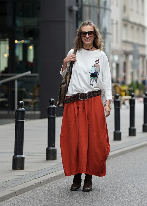 Ceglana spódnica maxi typu bombka z elastycznym pasem i przeszyciami, zestawiona z jasną bluzką i botkami w miejskiej stylizacji.