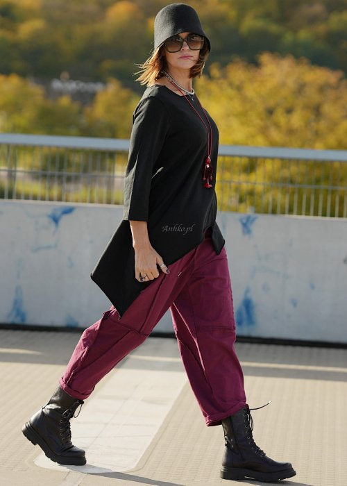 Bordowe spodnie dresowe damskie z obniżonym krokiem i ozdobnymi przeszyciami, luźny fason z gumką w pasie i sznurkiem, stylizacja miejska z czarnymi botkami.