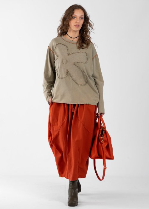 Ceglana spódnica maxi typu bombka z elastycznym pasem i przeszyciami, zestawiona z jasną bluzką i botkami w miejskiej stylizacji.