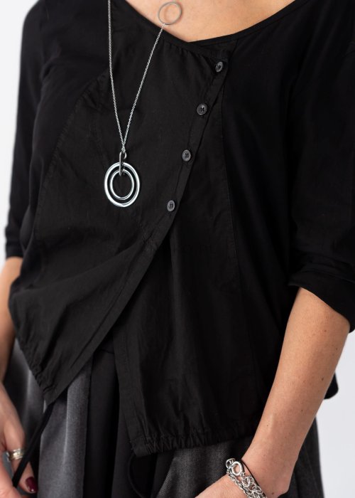 Czarna bluzka damska z asymetrycznym dekoltem odsłaniającym ramię i guzikami, stylizowana z elegancką spódnicą w minimalistycznym looku.