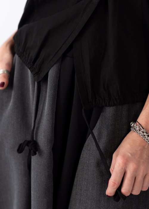 Czarna bluzka damska z asymetrycznym dekoltem odsłaniającym ramię i guzikami, stylizowana z elegancką spódnicą w minimalistycznym looku.