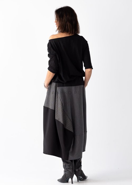 Czarna bluzka damska z asymetrycznym dekoltem odsłaniającym ramię i guzikami, stylizowana z elegancką spódnicą w minimalistycznym looku.